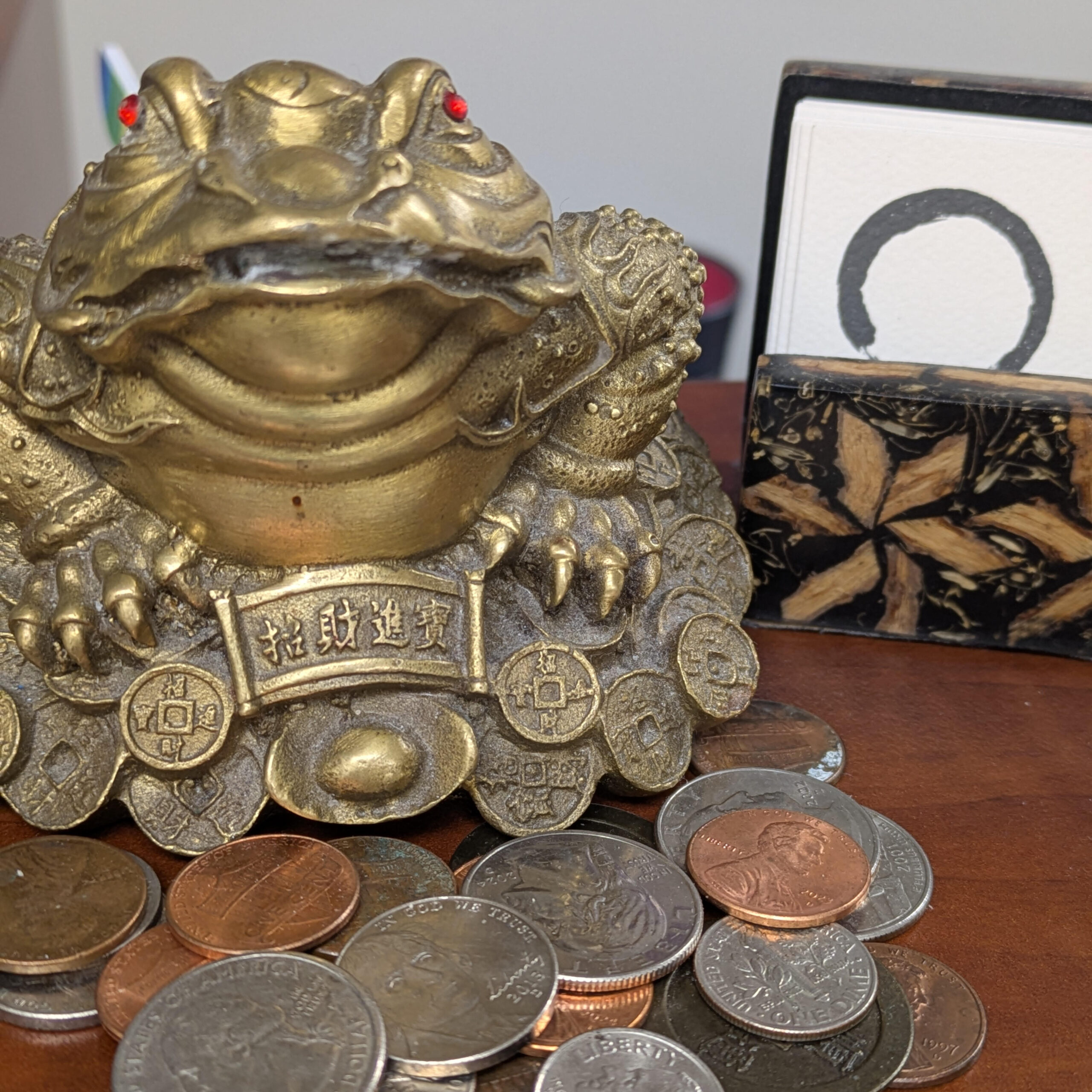 Lucky brass frog on a table with a pile of coins and a business card holder